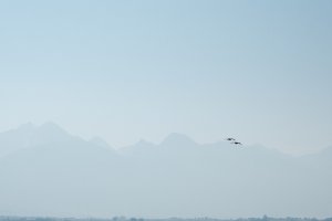landscape of the mission mountains taken from ninepipes reservoir during mid-morning, the sky thick with smoke, a pair birds flying from right to left