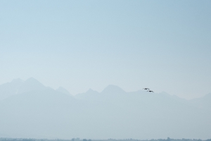 landscape of the mission mountains taken from ninepipes reservoir during mid-morning, the sky thick with smoke, a pair birds flying from right to left