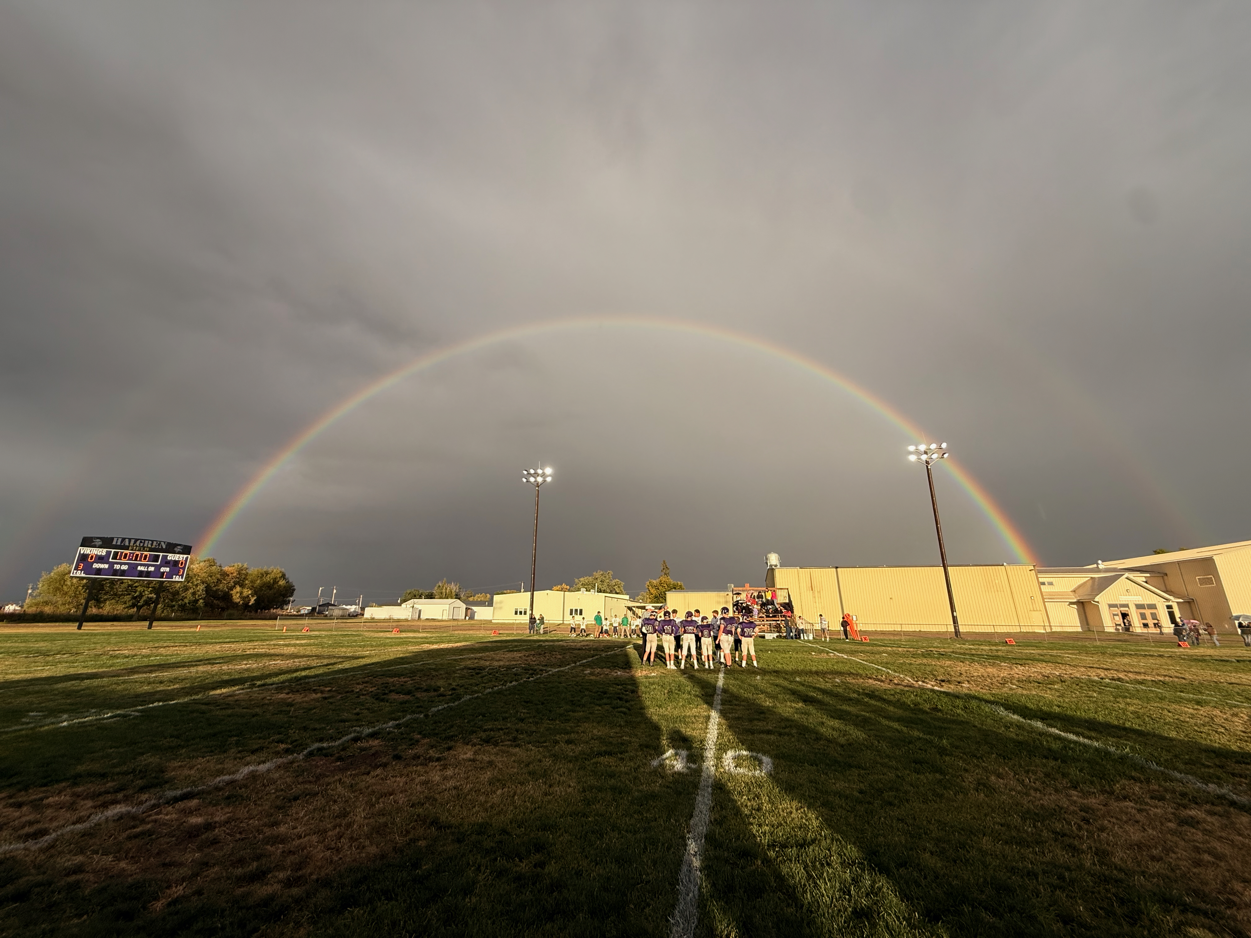 Football players on a field under a double rainbow a few moments before kickoff