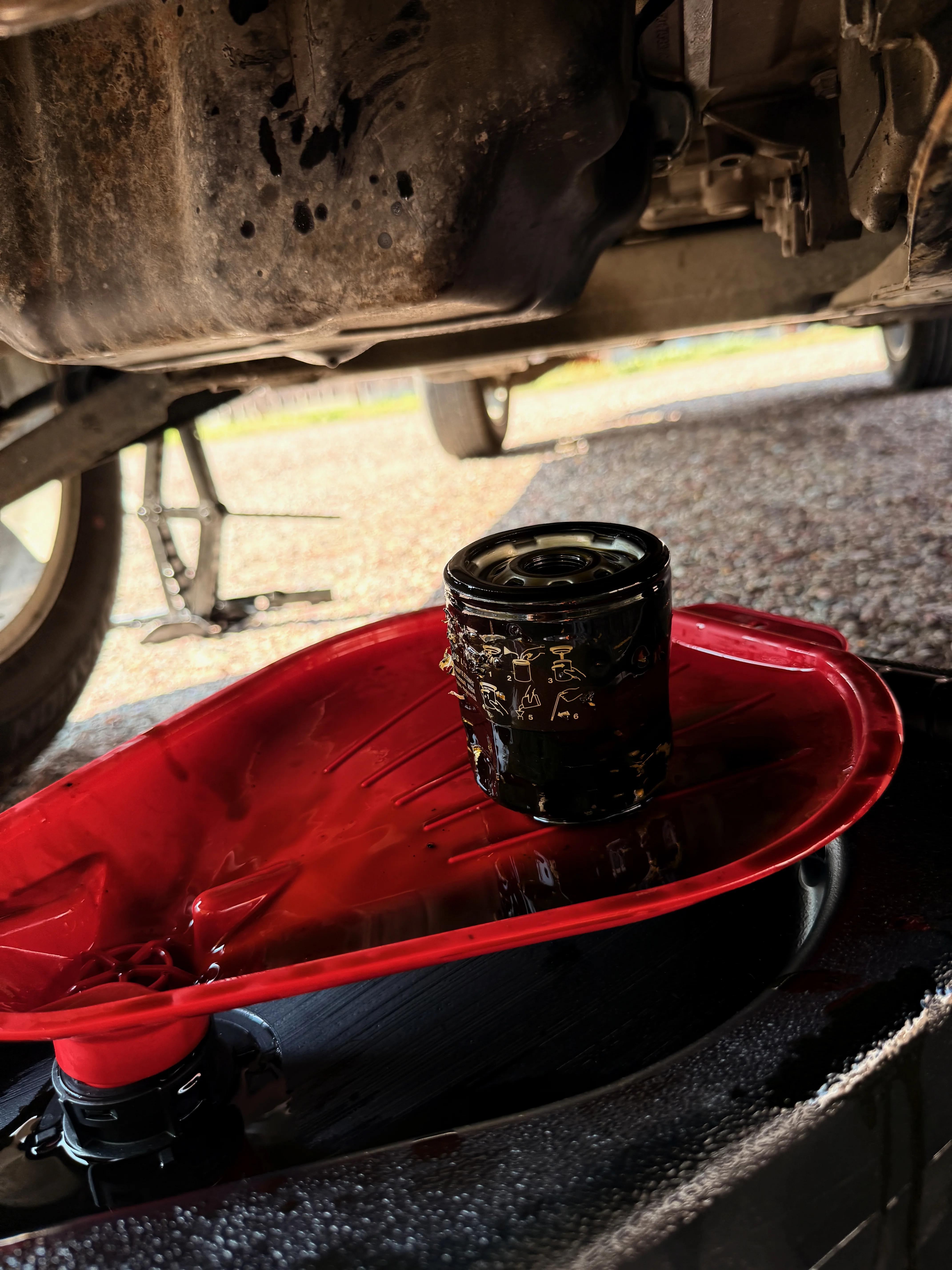 The same oil pan now holds the old oil filter as it slowly drains into the pan.